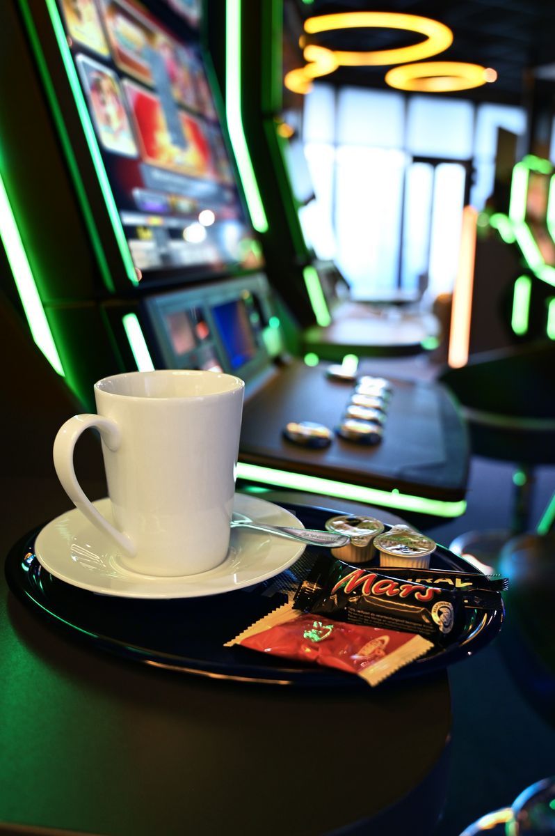 Kleines Tableau mit weißer Tasse und drei kleinen Schokoriegeln, steht auf einem Spielautomaten.